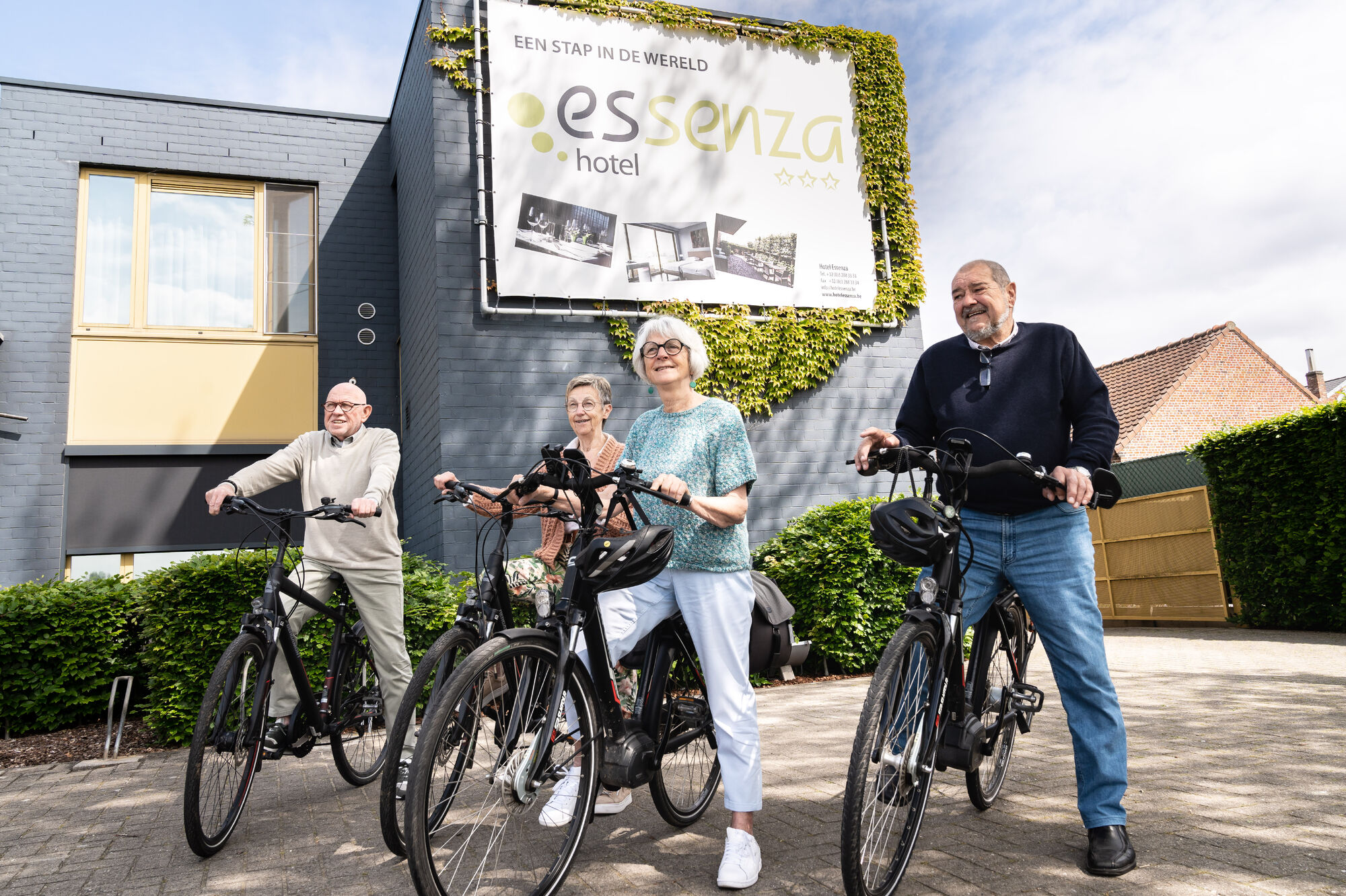 Vier mensen met een fiets aan hotel Essenza