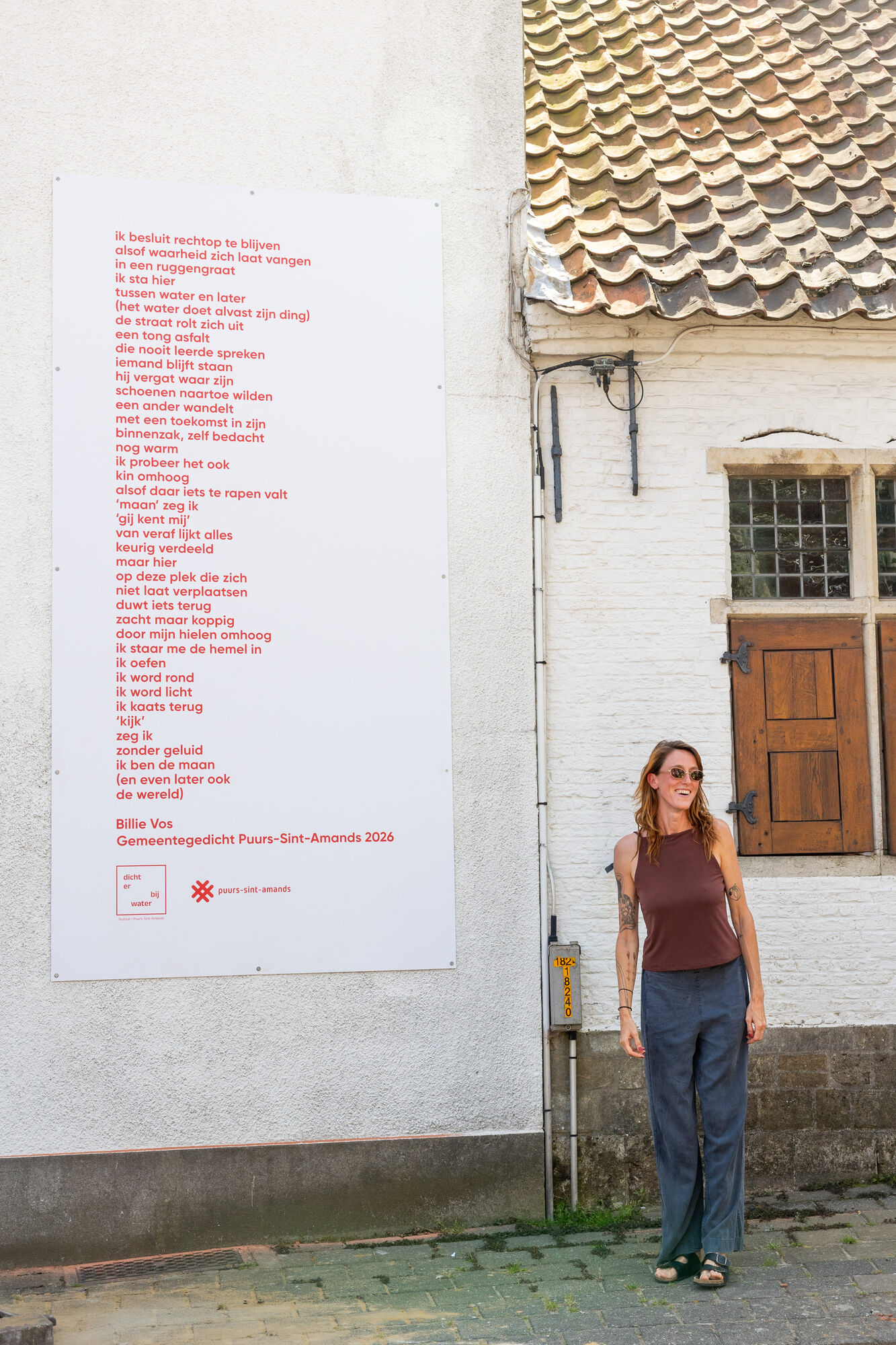 Billie Vos naast haar nieuwe gemeentegedicht in het straatbeeld van Sint-Amands