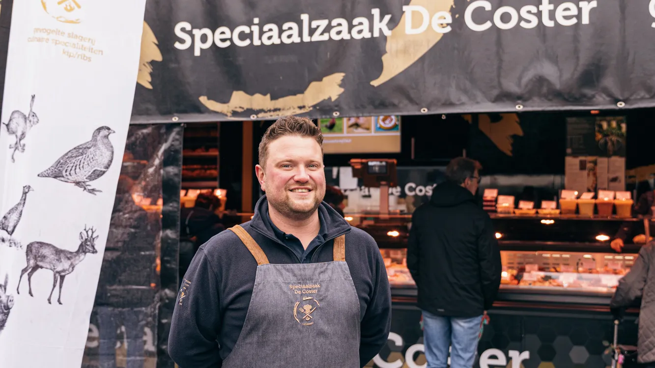 Marktkramer Gill De Coster poseert voor zijn kraam op het Kerkplein van Puurs